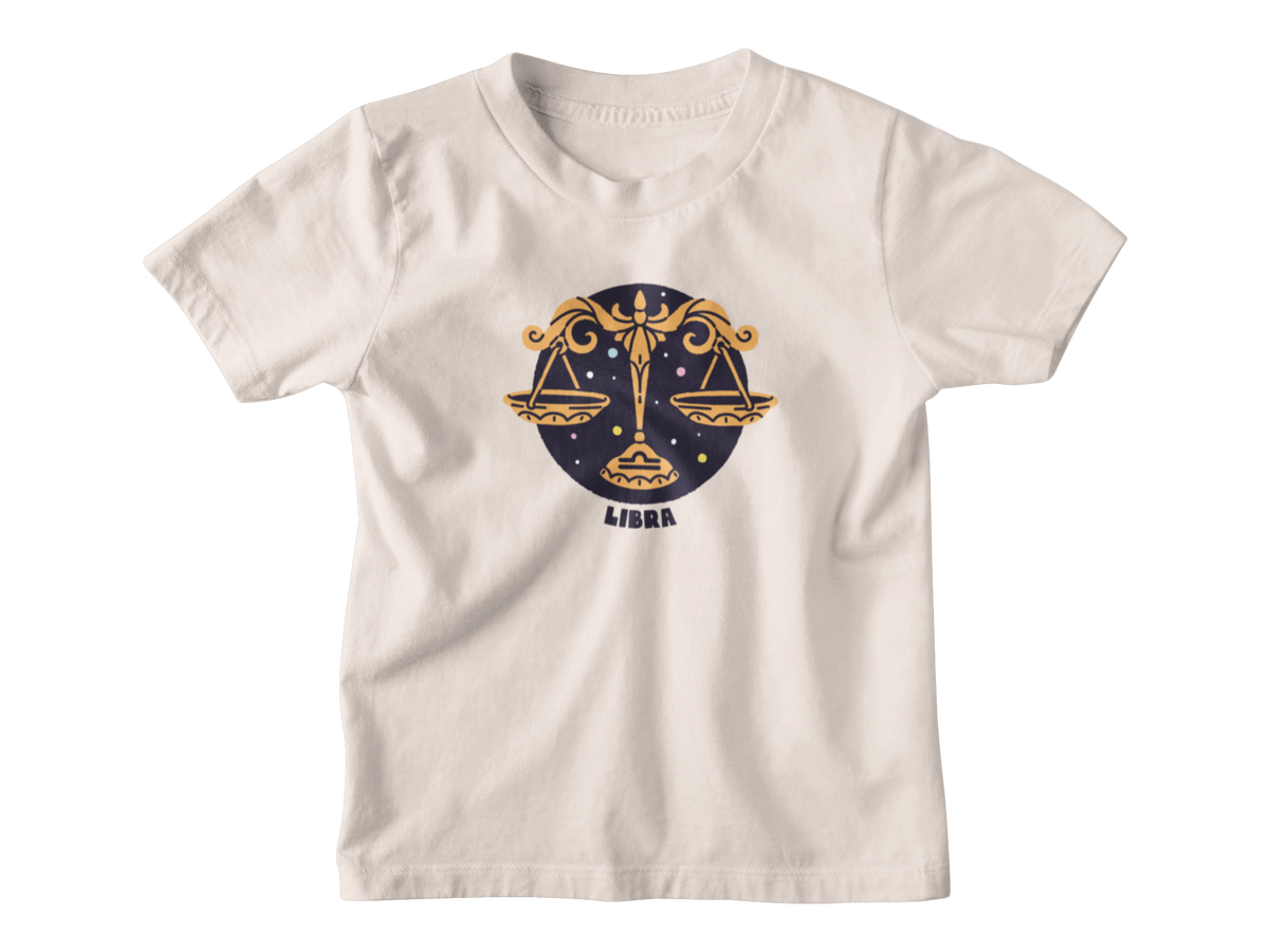 A light yellow short-sleeve t-shirt with a Libra zodiac graphic on the chest, featuring a gold scale of justice design over a dark blue circle with the word &