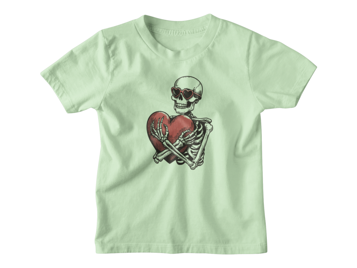 A light green Halloween short-sleeve kids t-shirt with a graphic of a skeleton wearing sunglasses and holding a broken red heart, displayed on a clean white background.