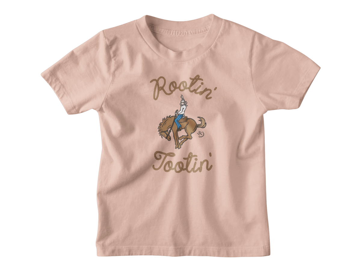 A light peach-pink kids short-sleeve t-shirt with a graphic of a cowboy riding a bucking horse, surrounded by the words &