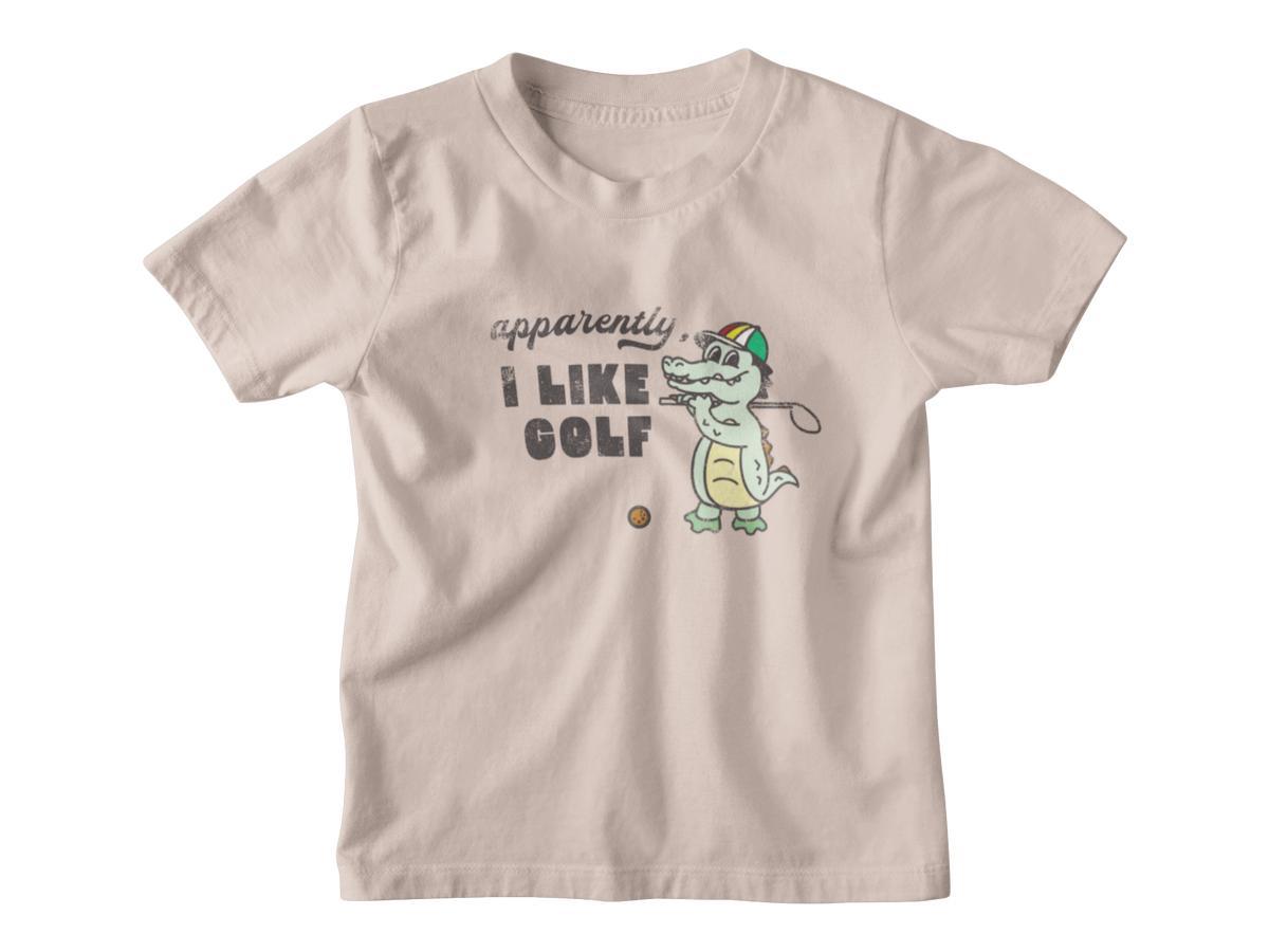 A light beige short-sleeve t-shirt with a graphic print of a cartoon alligator wearing a green and yellow golf hat, holding a golf club, with the text &