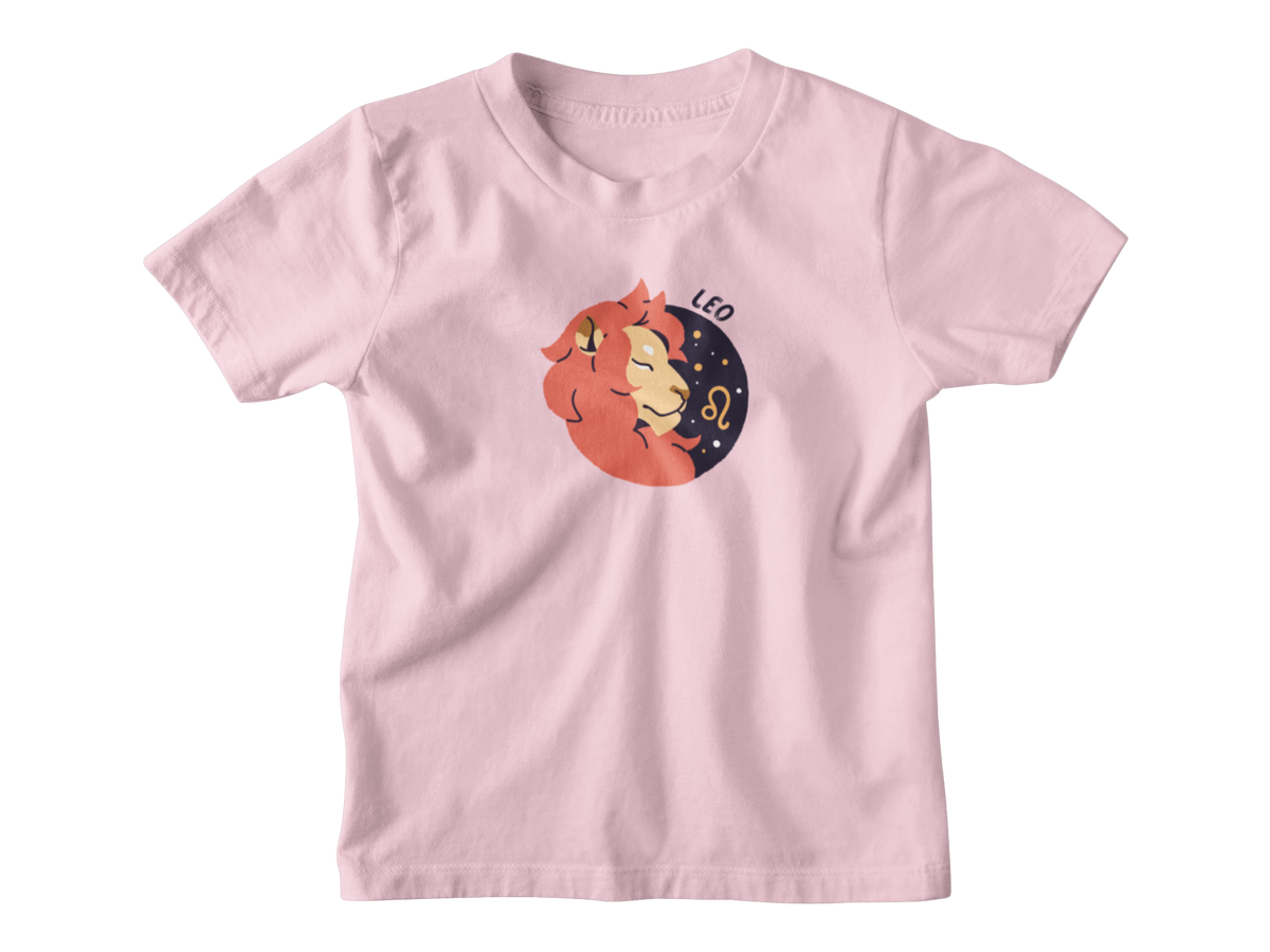 A pink short-sleeve crewneck t-shirt featuring a cartoon graphic of a Leo zodiac sign, showing a sleeping orange lion resting on a dark blue crescent moon with stars and the text &