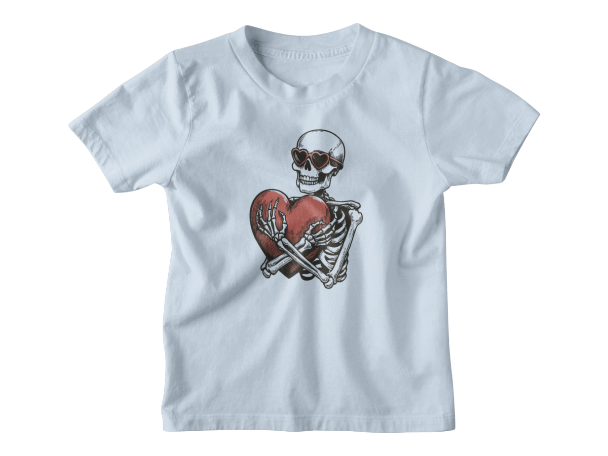 A light blue Halloween short-sleeve kids t-shirt with a graphic of a skeleton wearing sunglasses and holding a broken red heart, displayed on a clean white background.
