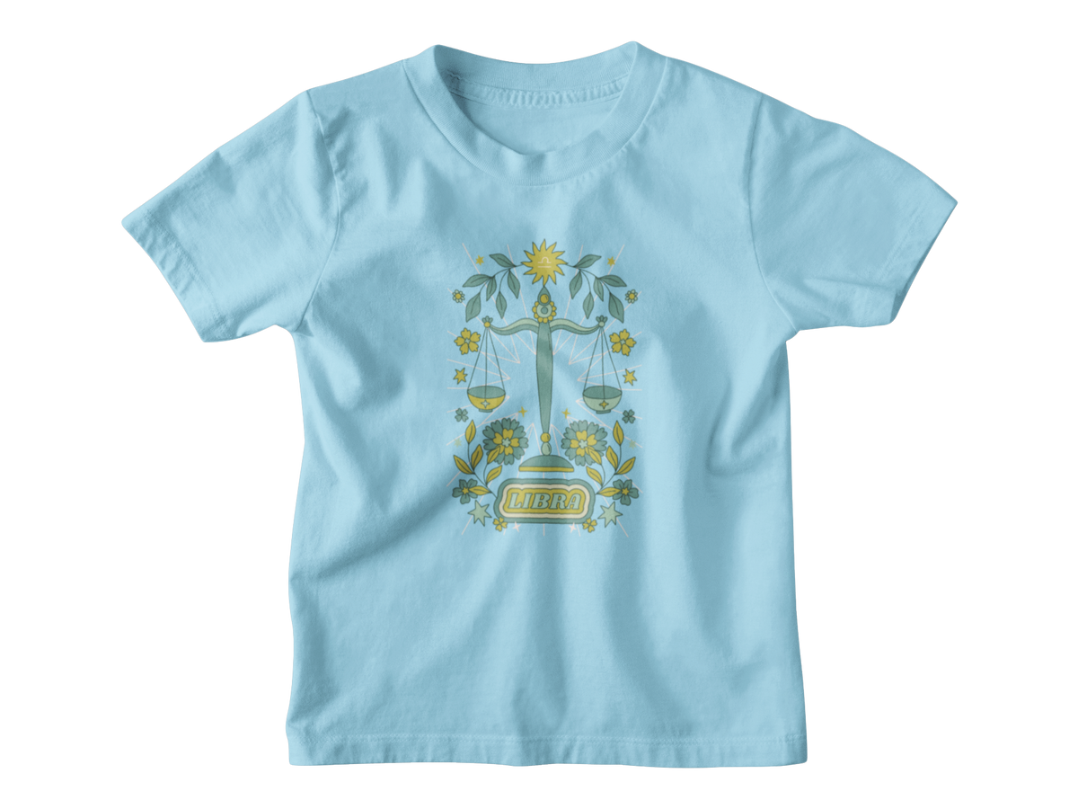 A light blue short-sleeve kids t-shirt with an astrology graphic of a green and gold scale of justice surrounded by floral elements and the word &