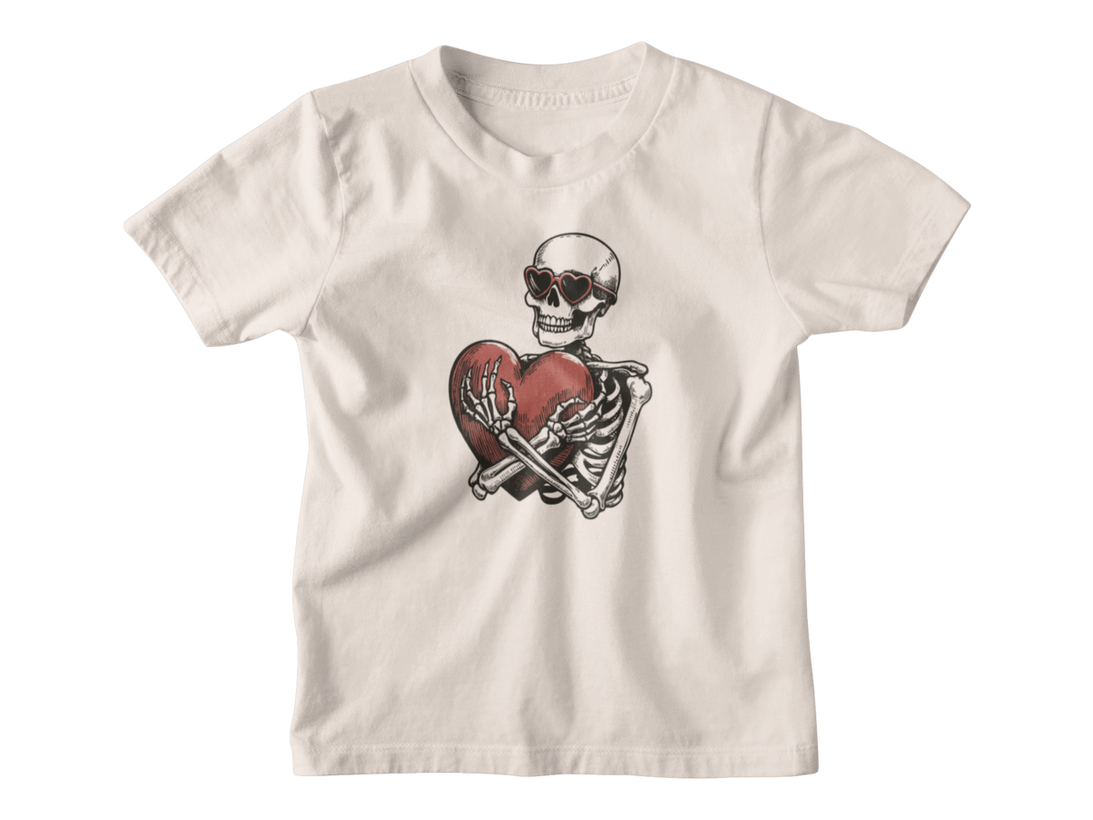 A cream-colored short-sleeve t-shirt with a graphic of a skeleton wearing sunglasses and holding a red heart, displayed on a clean white background.