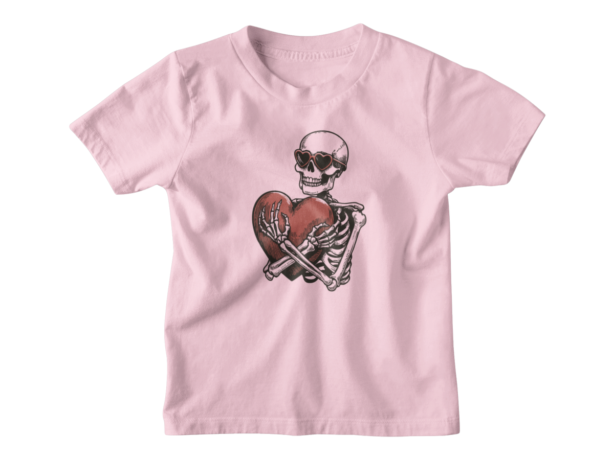A light pink short-sleeve kids t-shirt with a graphic of a skeleton wearing sunglasses and holding a broken red heart, for Halloween or Valentine&