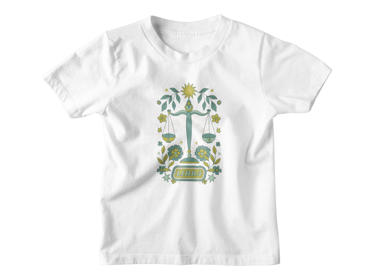 A white pink short-sleeve kids t-shirt with an astrology graphic of a green and gold scale of justice surrounded by floral elements and the word &