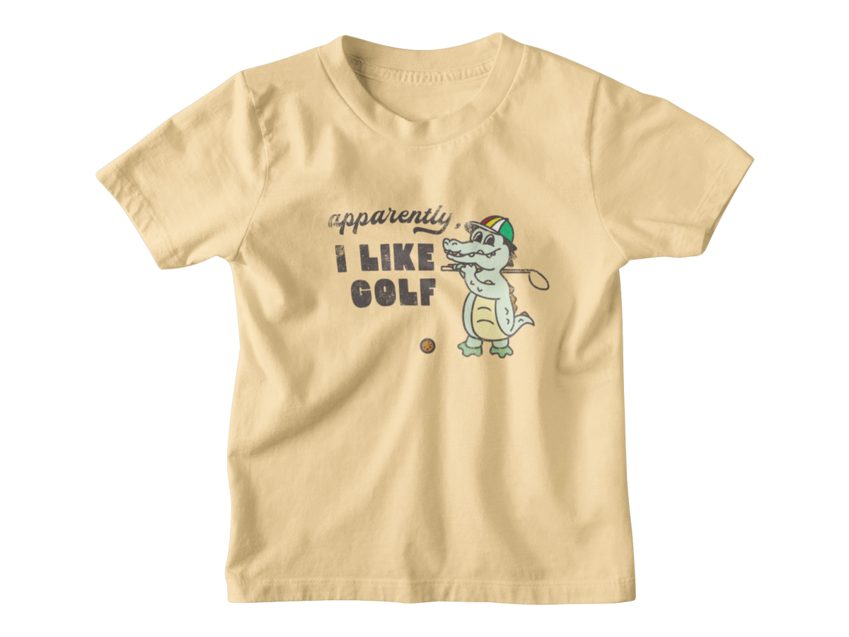 A light beige kids short-sleeve t-shirt with a graphic print of a cartoon alligator playing golf, accompanied by the text &
