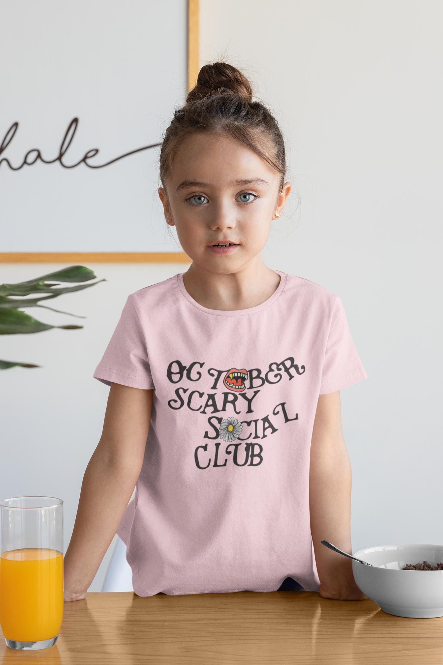 Young girl wearing a pink t-shirt with text of October Scary Social Club for Halloween.