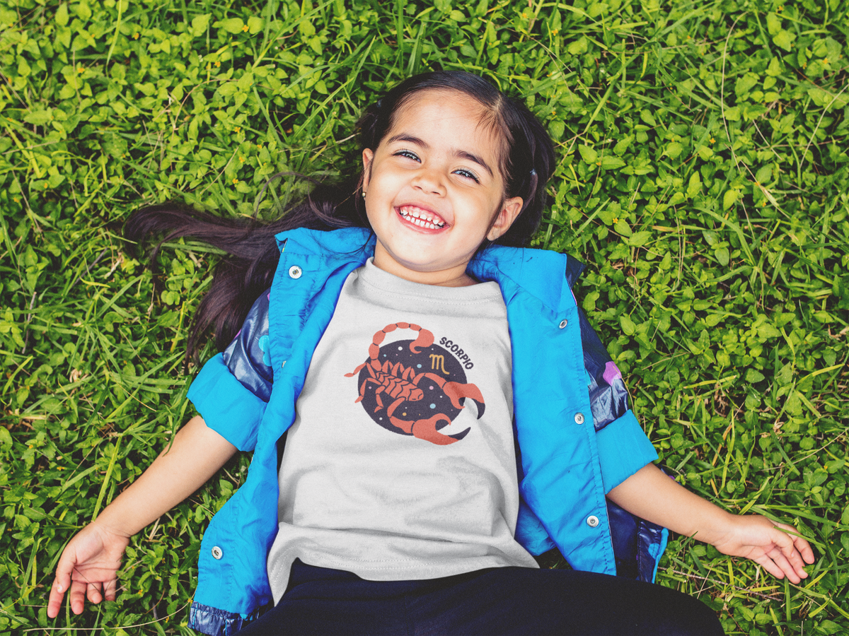 A photo of a kid wearing a Scorpio astrology shirt laying in the grass.